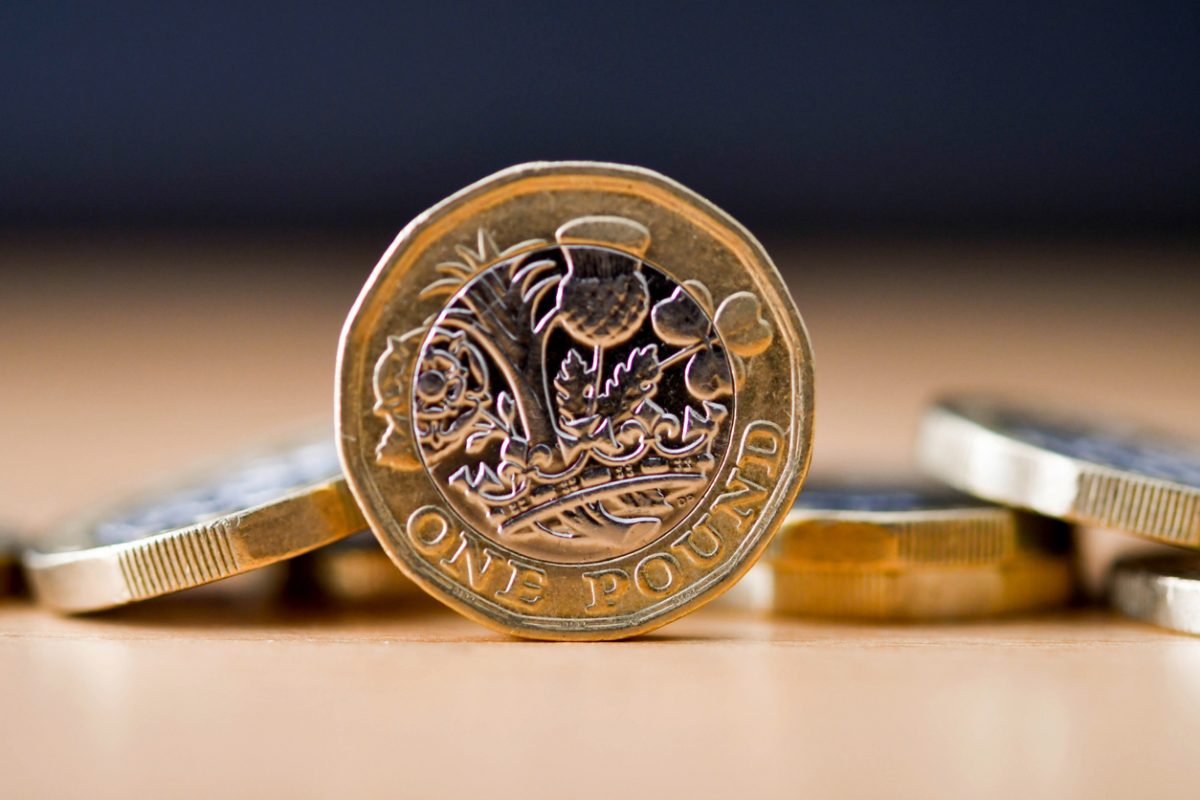 British one pound coin standing on its edge with other coins in the baclground. No people.