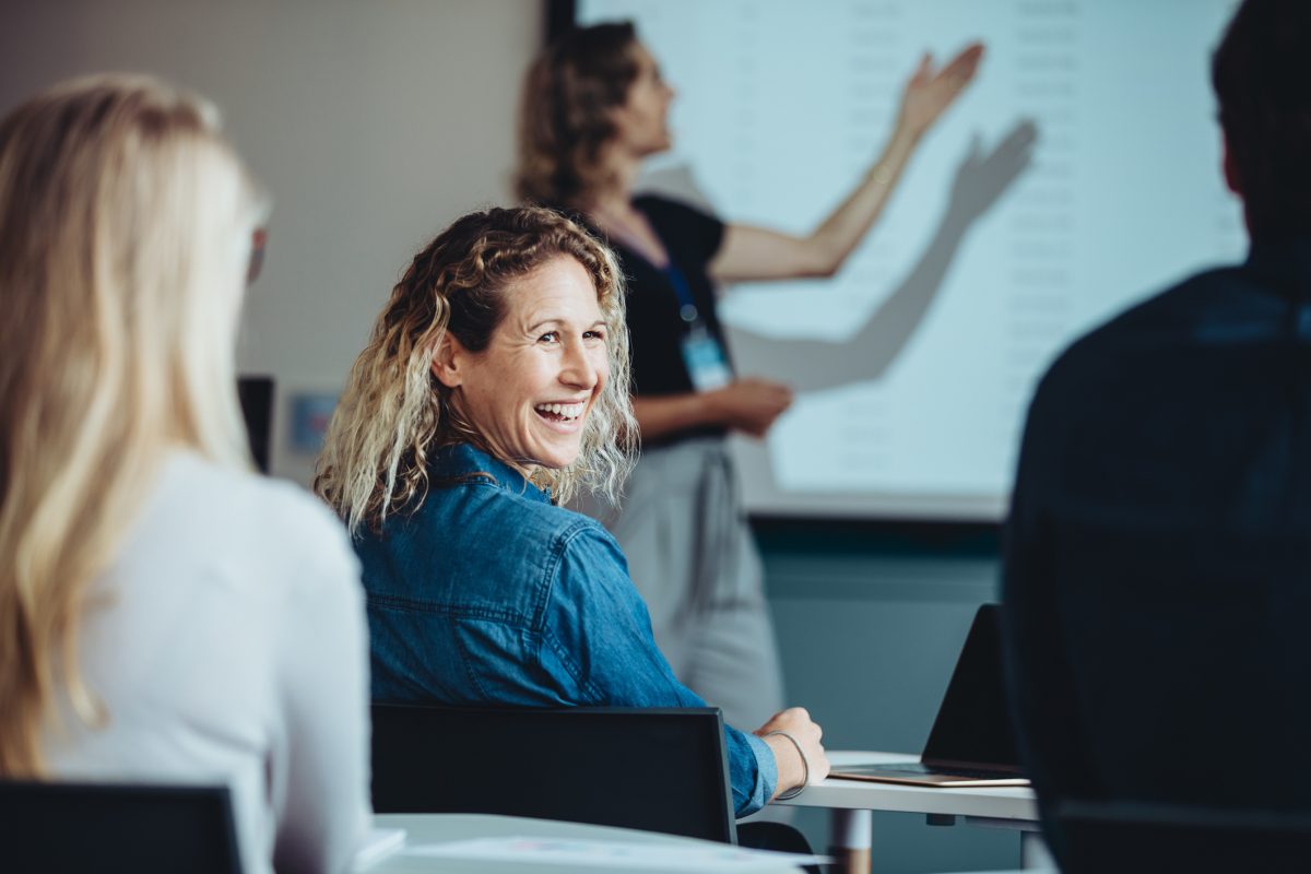 Rear view of a woman sitting in audience looking back at a colleague and smiling during a conference. Businesswoman smiling during a presentation.