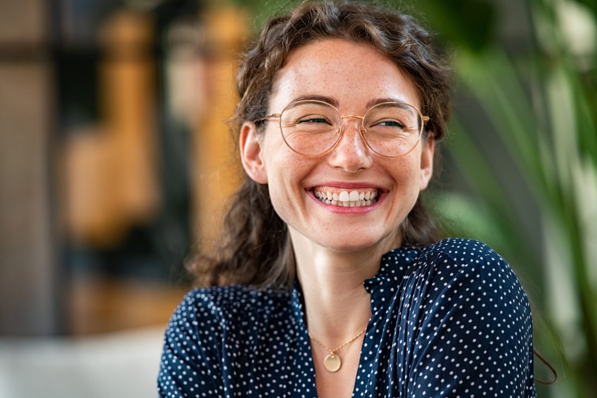 Portrait of laughing young woman wearing spectacles in office. Carefree casual girl wearing glasses and looking away. Confident beautiful student wearing specs and smiling.