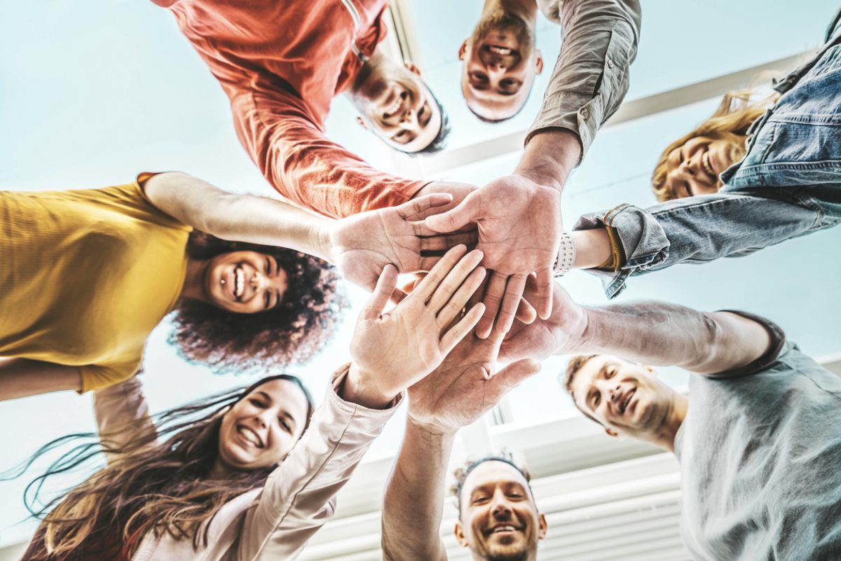 Group of young people stacking hands together outdoor - Community of multiracial international people supporting each other - Union, support and human resources concept