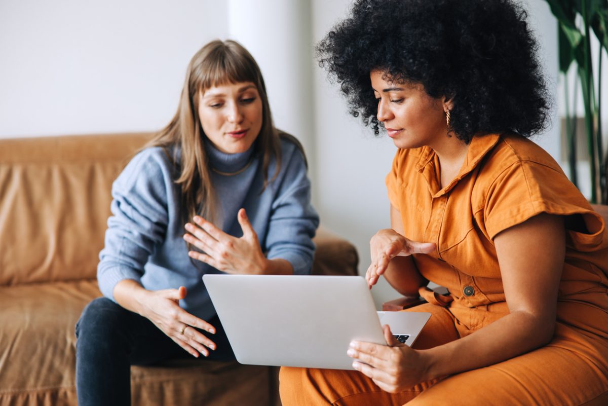 Two young businesswomen having a discussion while looking at a laptop screen. Two female entrepreneurs working as a team in a modern workplace.